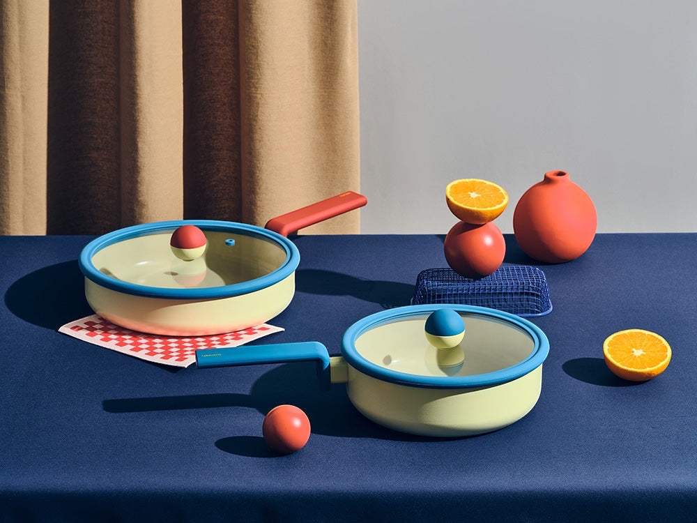 Neoflam Danish cookware set: a pastel yellow 20cm stockpot with blue rim and red/yellow knob, and a matching wok. Both have glass lids.