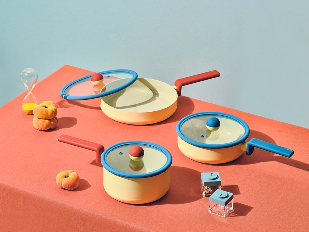 Neoflam Danish cookware set with a yellow stockpot and wok, featuring blue rims and red and blue handles. Includes glass lids with colorful knobs.